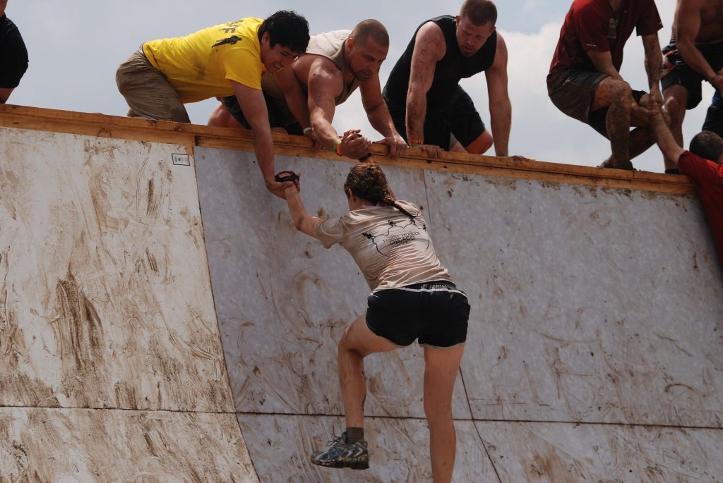 A group working to pass a hurdle on a mud run race