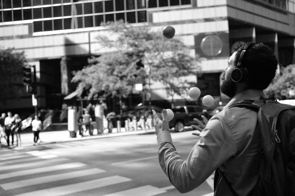 A man attempting to juggle & listen to music as he crosses the road